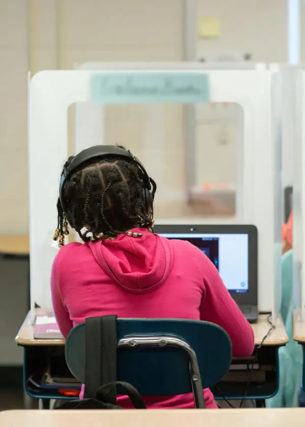 A fifth-grade student works on her laptop behind a personal protection shield at Wesley Elementary School. <br><strong> Photo by Allison Shelley for American Education: Images of Teachers and Students in Action </strong>