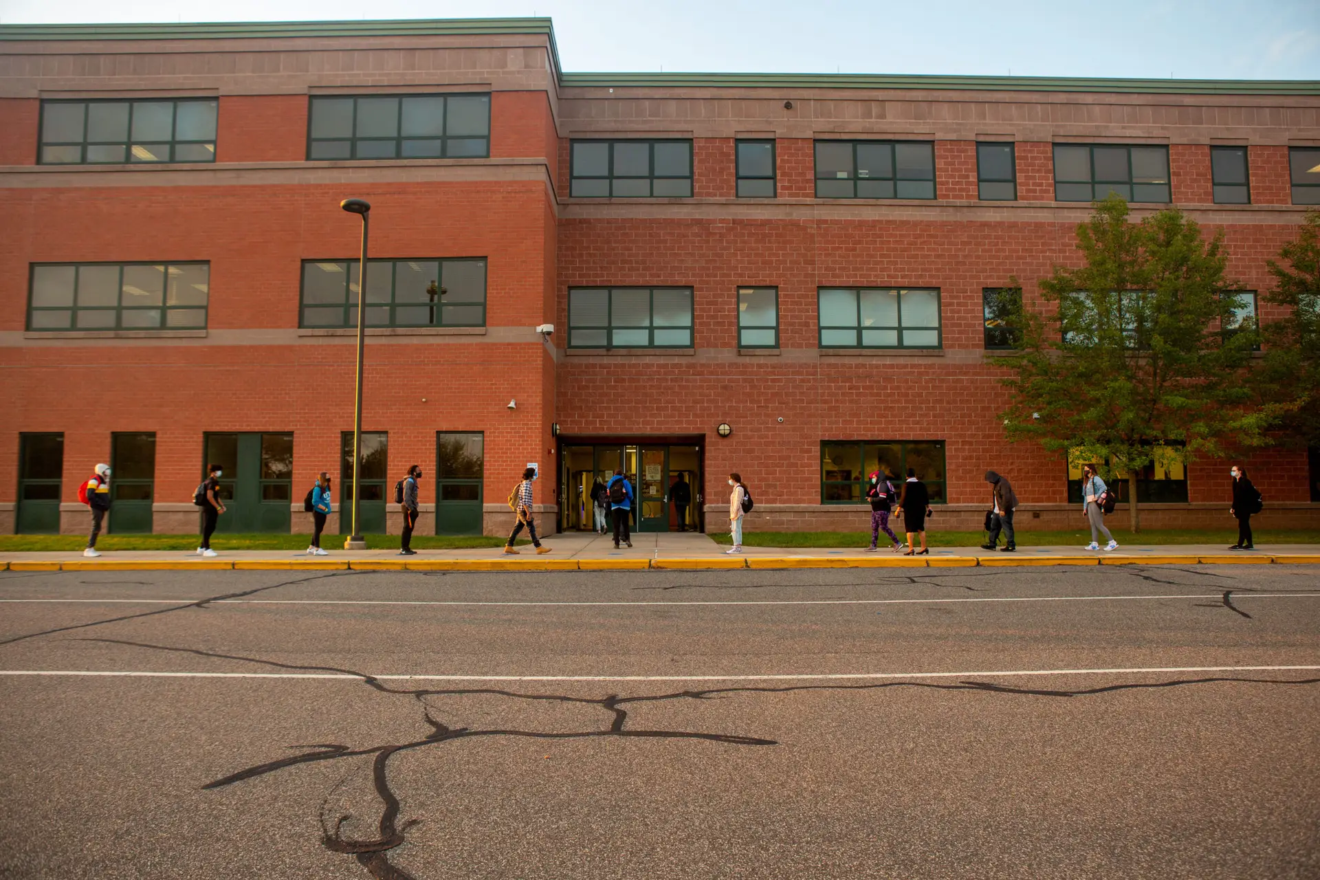 Students line up on socially distanced dots painted on the sidewalk to wait their turn to have their temperatures checked before entering Middletown High School.